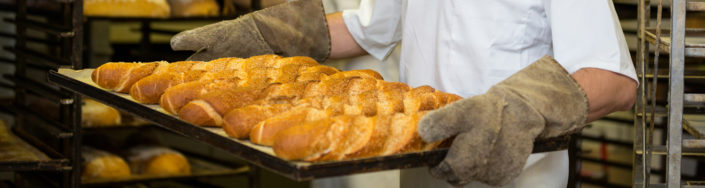 Smiling baker carrying a tray of freshly baked french baguette